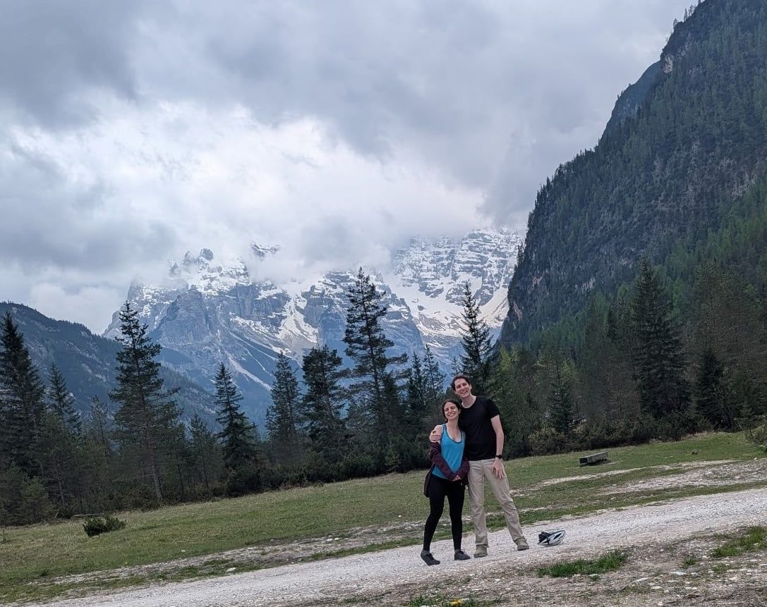 Katherine and Johnny on a gravel track below the snow-covered Dolomites, cloud sitting on the peaks