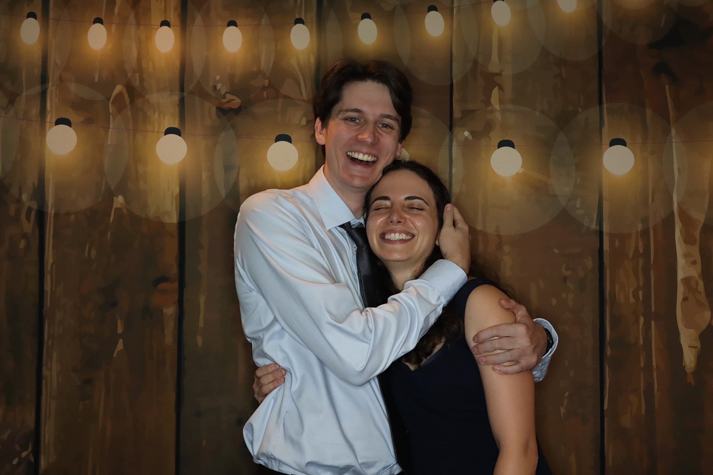 Katherine and Johnny in front of a lit wooden wall at Evan and Stef's wedding