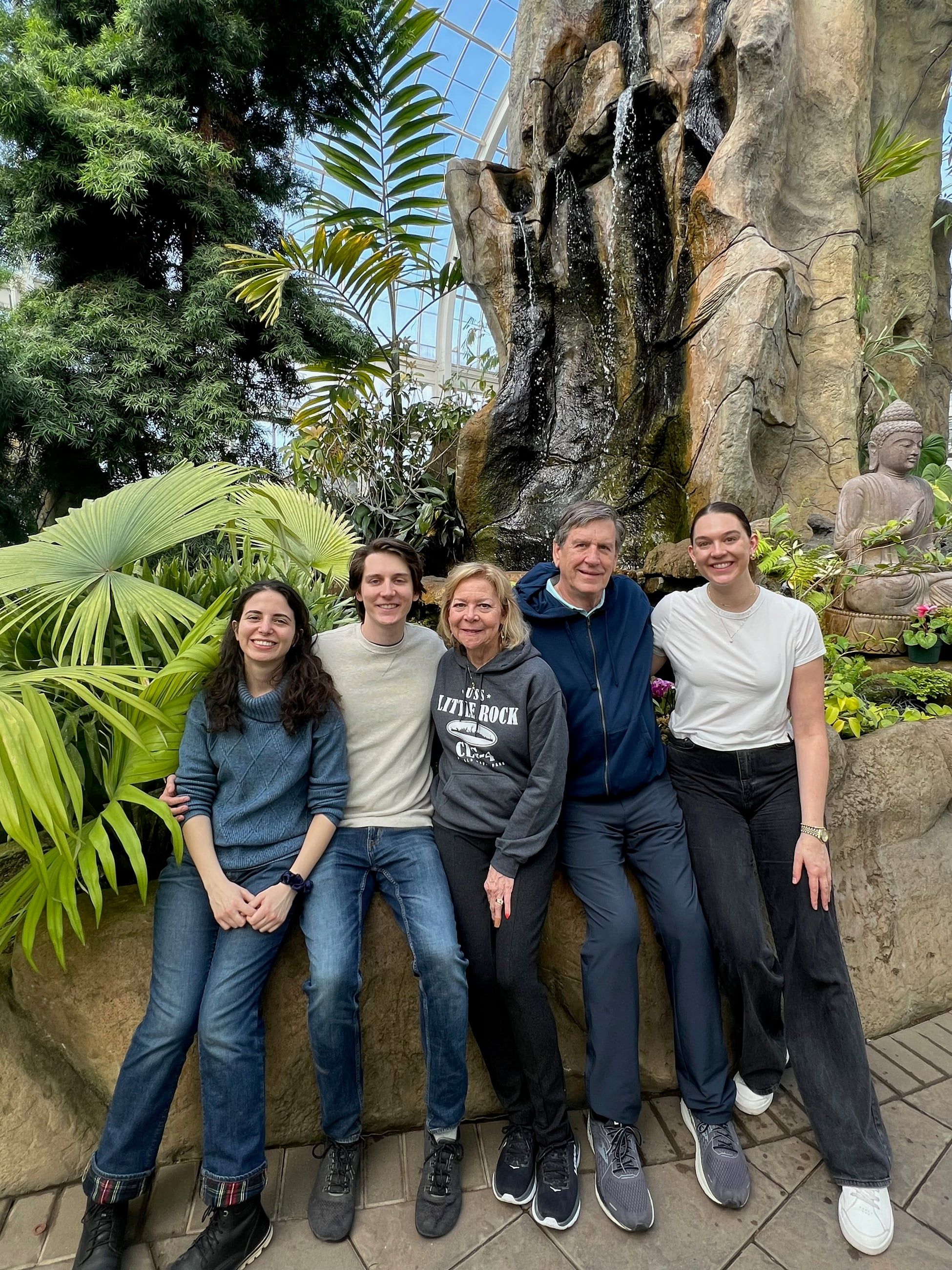 Katherine, Johnny and family in a glasshouse of palms and ferns, a waterfall behind them