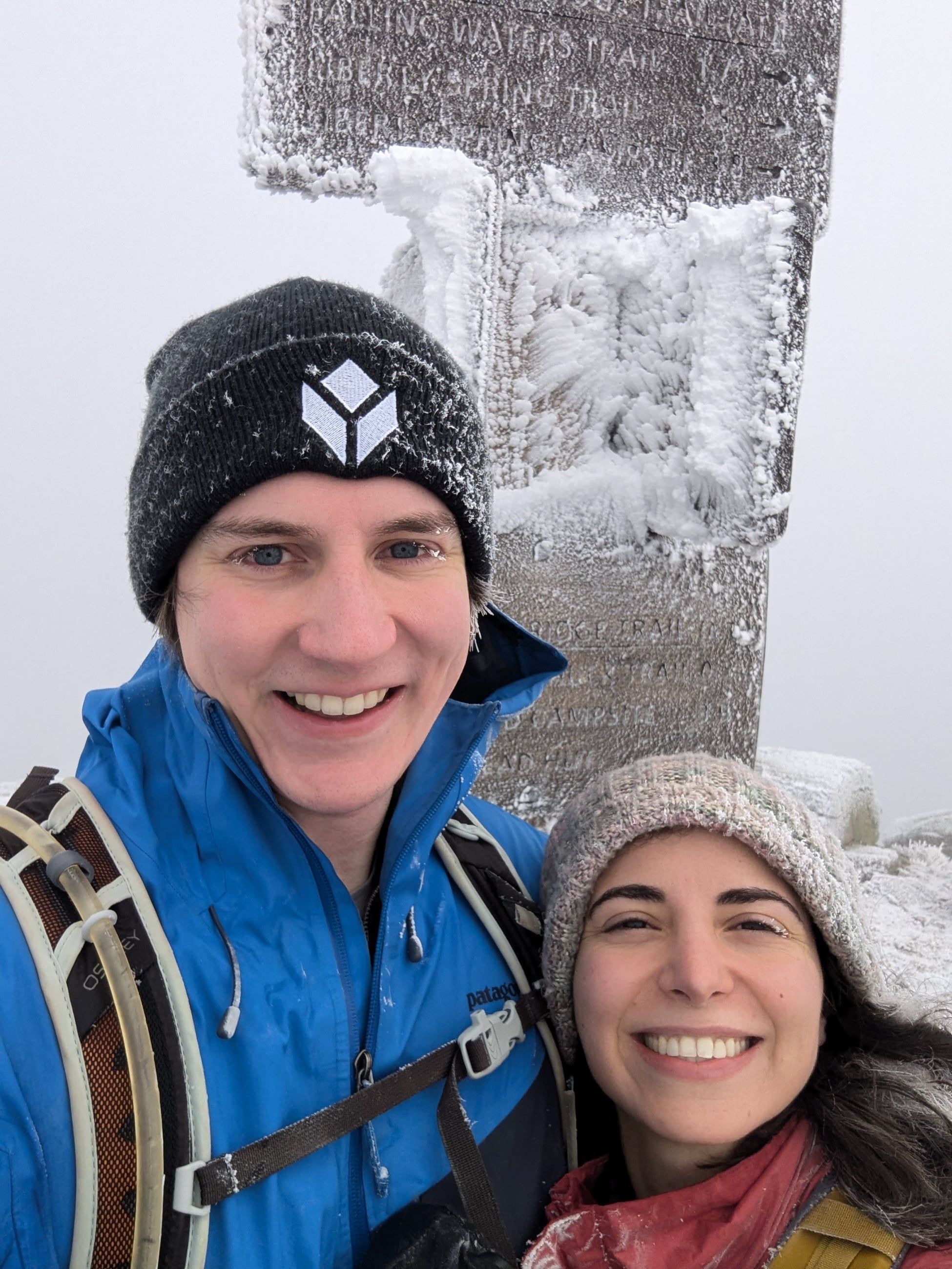 Katherine and Johnny bundled up beside a rime-covered summit sign on Lafayette