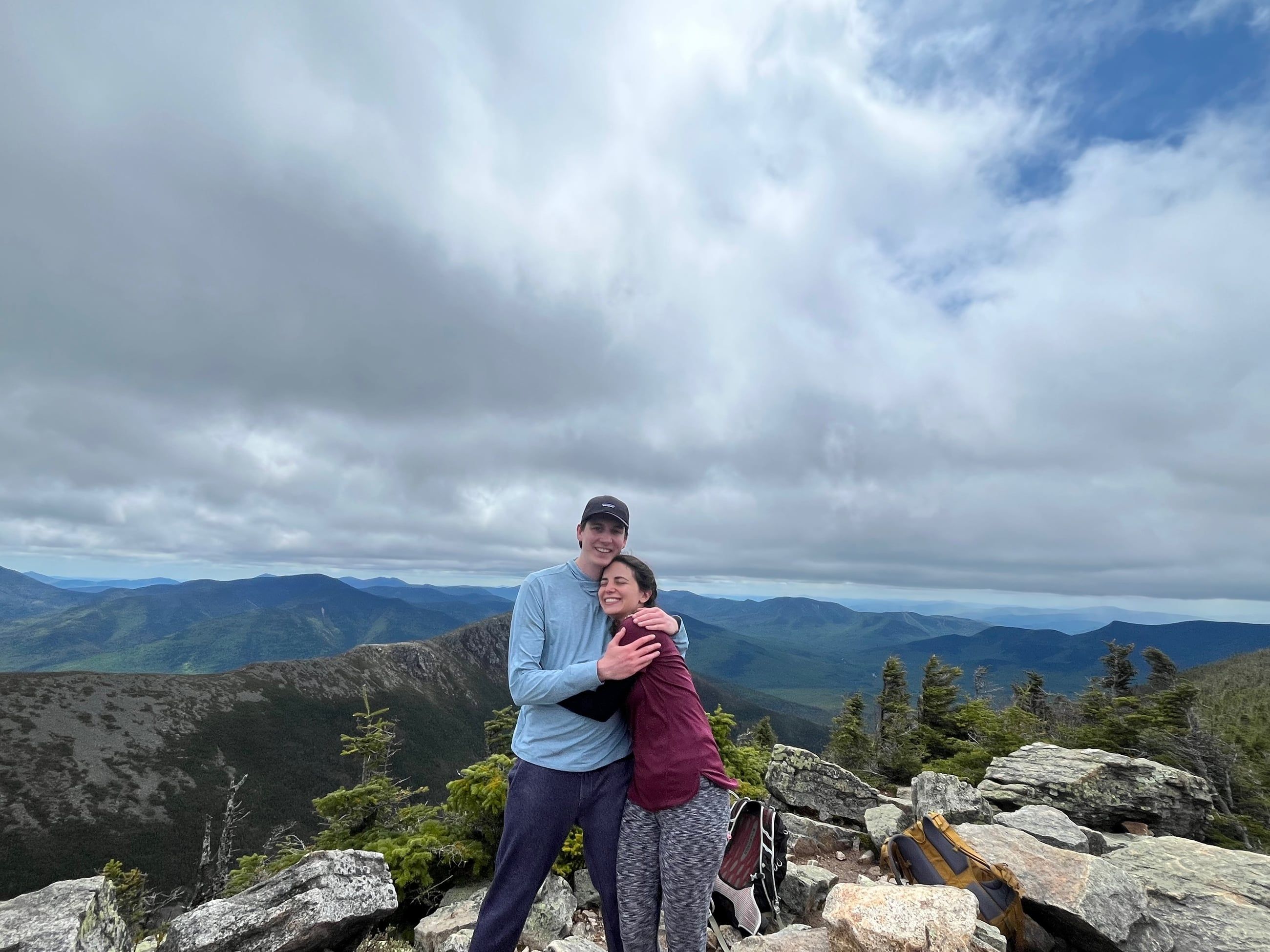 Katherine and Johnny holding each other on the rocky summit of West Bond, ridges running out behind them